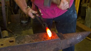 Blacksmith beating white hot iron with hammer on anvil.