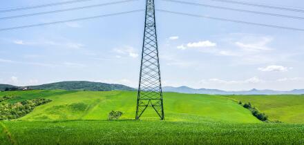High voltage power line tower standing in a lush green field in Tuscany. Modern infrastructure in a rural spring landscape near Volterra, Italy