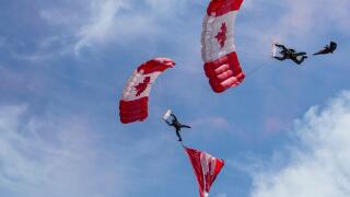 Canadian parachute jumpers perform at the Calgary Stampede and Rodeo. Red and white parachutes with maple leaf design against blue sky with wispy clou