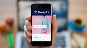 A man looks at his iPhone which displays the Trustpilot logo (Editorial use only).