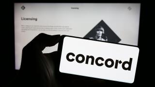Person holding smartphone with logo of US creative rights company Concord Music Group Inc. in front of website. Focus on phone display.