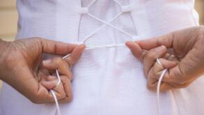 A woman tightening laces on back of her white dress.