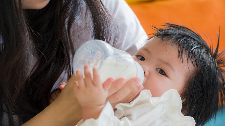 lifestyle candid portrait of young happy and sweet Asian Chinese woman feeding her beautiful baby girl with formula bottle at holidays resort as mothe