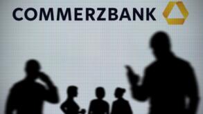 The Commerzbank logo is seen on an LED screen in the background while a silhouetted person uses a smartphone in the foreground (Editorial use only)