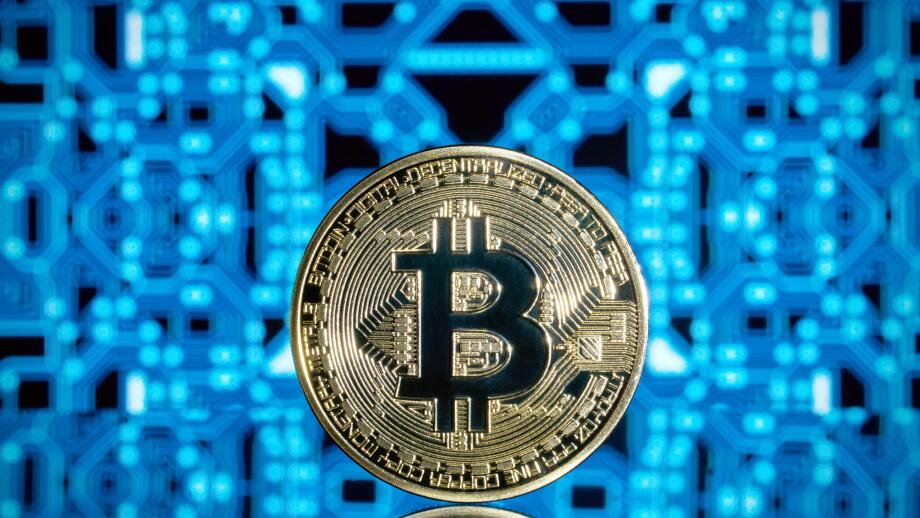 Standing golden bitcoin crypto currency blockchain coin against a blue reflective circuit board background