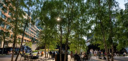 London, UK: Exchange Square at Broadgate, an open space in the City of London. People sit in the square and evening sunlight filters through the trees