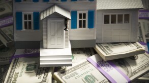 Toy house on pile of one hundred dollar bills