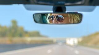 Woman driving a car on a motorway with a view ahead through the windscreen and her glasses reflected in the rear view mirror