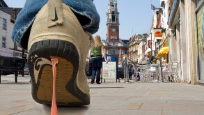 Close up of Bubble gum stuck to trainers. A pedestrian walking along a street gets discarded  gum stuck to his trainers