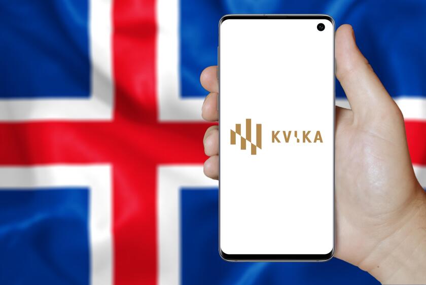 A man holds a smartphone displaying the logo of company Kvika banki listed on Nasdaq Iceland. Icelandic flag in the background. Credit: PIXDUCE