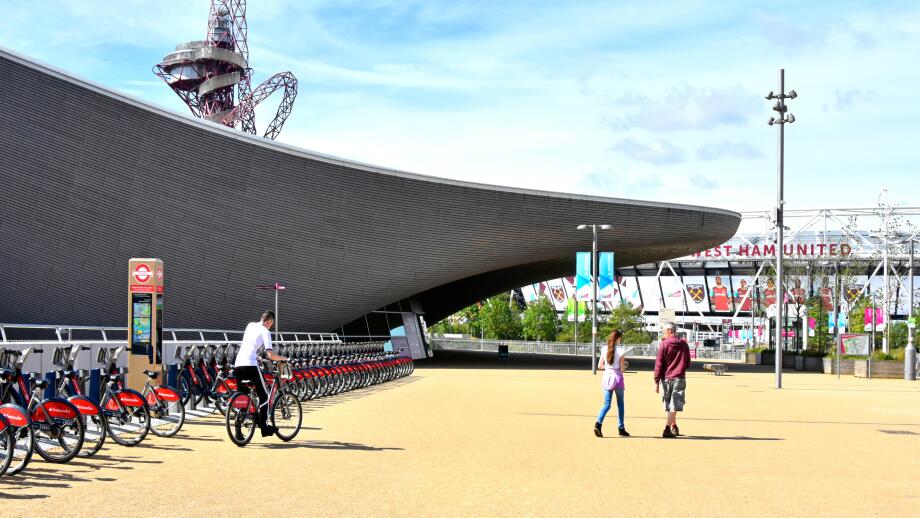 Person riding from Santander bike hire docking station at Aquatic Centre with Orbit Tower beyond in Queen Elizabeth Olympic Park Stratford London UK