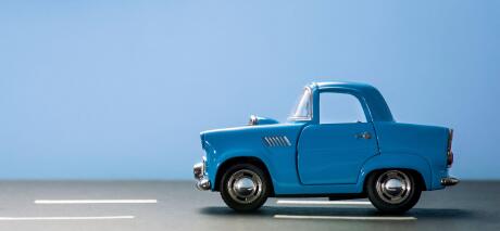Side view of a blue toy car on a blue background and on an asphalt road.
