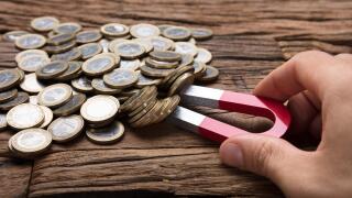 Cropped image of businessman's hand pulling coins with magnet on wooden table