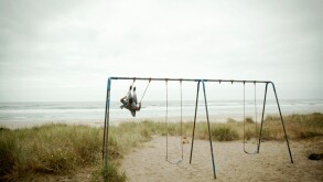 Female toddler watching father on beach swing
