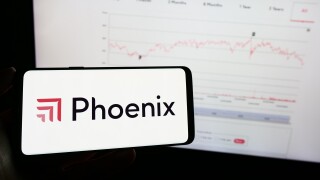 Person holding mobile phone with logo of British insurance company Phoenix Group Holdings plc in front of web page. Focus on phone display.