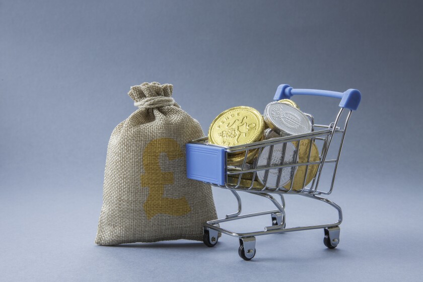 Supermarket shopping trolley full of UK currency, cash, coins and money representing consumer spending with copy space