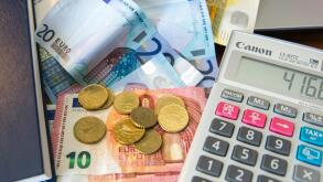 Various Euro notes and coins with a calculator, diary and laptop computer.