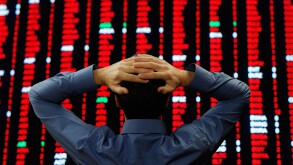 Stock Trader Stood in Front of a Large Display of Stock Prices