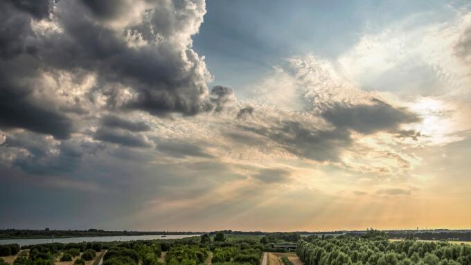 Dramatic skies with low sun and dark clouds approaching over the island of IJsselmonde and the Oude Maas river as seen from the artificial hill at Car