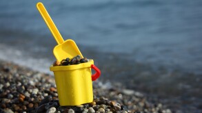 Yellow children's bucket full of pebble with  scoop on stone seacoast