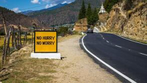 Roadside safety message sign "No Hurry, No Worry" on the Paro-Thimphu Highway in Bhutan on a sunny day