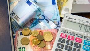 Various Euro notes and coins with a calculator, diary and laptop computer.