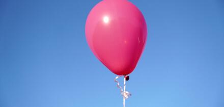 A single pink balloon against the blue sky in closeup