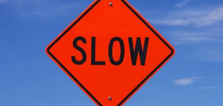 orange slow road sign with black letters in front of the sky