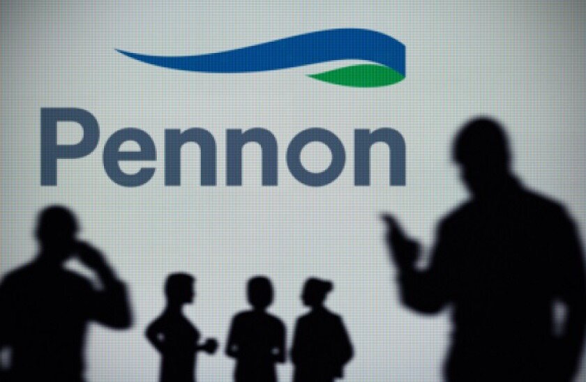 The Pennon Group logo is seen on an LED screen in the background while a silhouetted person uses a smartphone (Editorial use only)