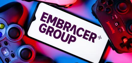 A smartphone with the Embracer Group logo on the screen surrounded by gamepads.