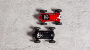 Red and black vintage toy cars racing on a grey surface