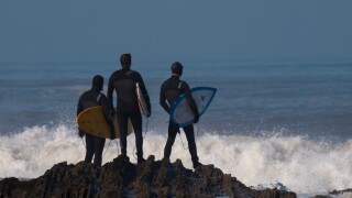 Surfers standing on rocks looking out to sea, Westward Ho!, Devon, UK