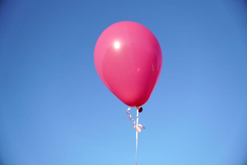 A single pink balloon against the blue sky in closeup