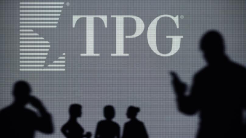 The TPG Capital logo is seen on an LED screen in the background while a silhouetted person uses a smartphone (Editorial use only)