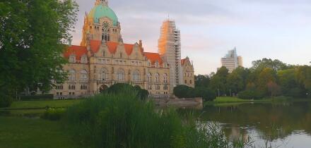 Rear view of Hannover City Hall with a reflective pond and surrounding park landscape.