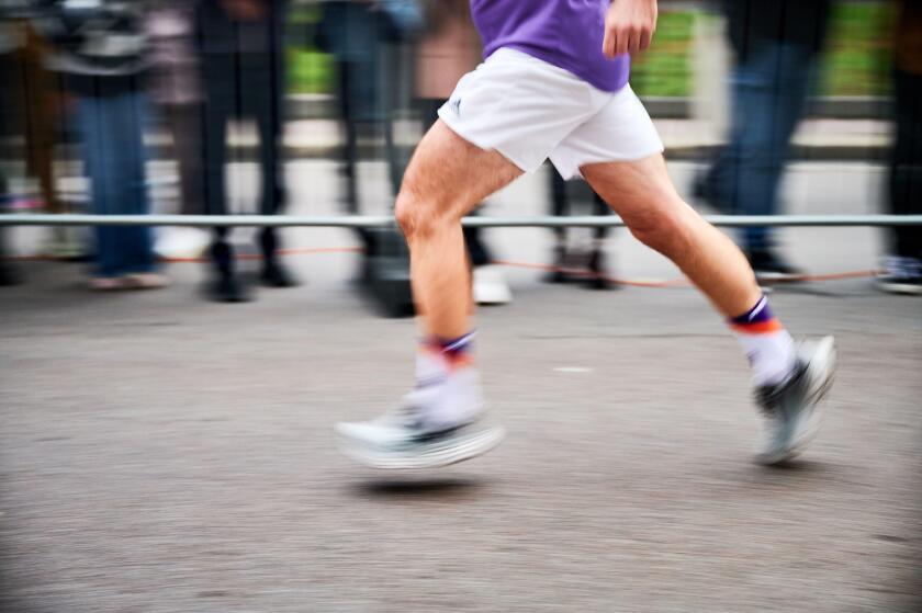 Close-up shot of runner's legs in motion, showing powerful stride as race down street, with blurred spectators in background emphasizing speed and intensity of moment.
