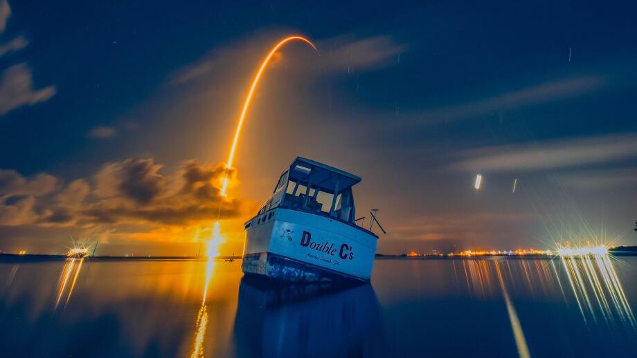 A Falcon 9 ascends to space behind a grounded boat on the Banana River in Florida in July 2024.