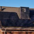 A modern, energy-efficient house in Assen, Netherlands, featuring integrated heat pumps on the roof, solar panels, and a clear blue sky.