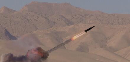 Fighting in a desert area. A missile soars into the sky, leaving a trail of smoke behind it. Concept: military conflict in the Middle East