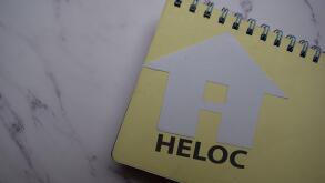 HELOC write on sticky note and house made from paper isolated on Office Desk.