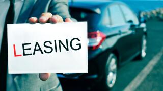 man in suit holding a signboard with the word leasing written in it, with a black car in the background