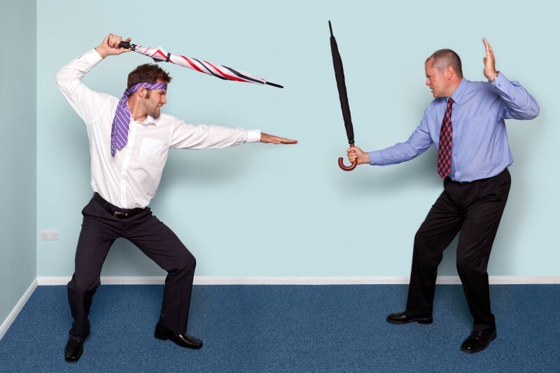 Photo of two businessmen having a sword fight using umbrellas, good image to convey conflict, rivalry or disagreement.