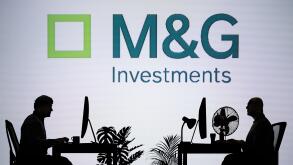 The M&G Investments logo is seen on an LED screen in the background while two silhouetted people work in an office environment (Editorial use only)