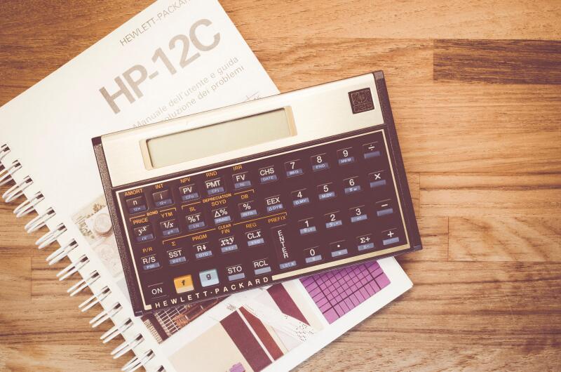 HP-12C Hewlett-Packard rpn financial calculator and manual on a natural wood table top background