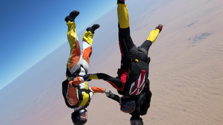 Skydiving team is holding hand together after they jumped out from a plane. Thereby they have fun and play in the blue sky.