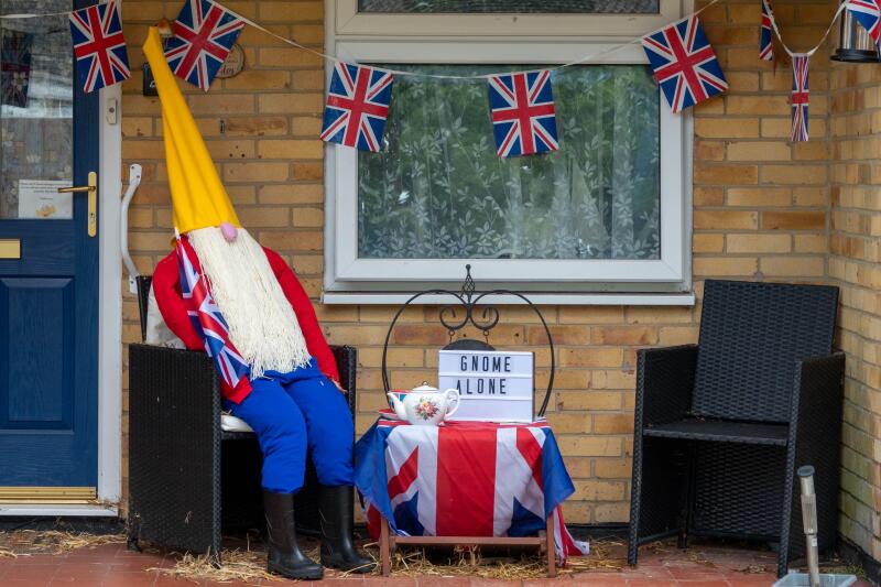 scarecrow dressed as gnome holding the union jack flag in celebration of the Queen's Platinum Jubilee and sign gnome alone