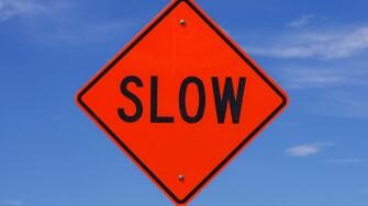 orange slow road sign with black letters in front of the sky