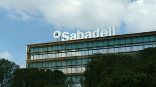 Barcelona, Spain - May 24, 2023: The multi-story building of Banco Sabadell stands against a cloudy sky, flanked by lush greenery in the foreground.