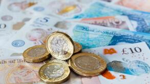 A pile of one pound £ coins British money sterling on new polymer £10 and £5 notes GBP close-up. England UK Britain