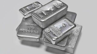 Silver bullion bars in a pile on plain grey background